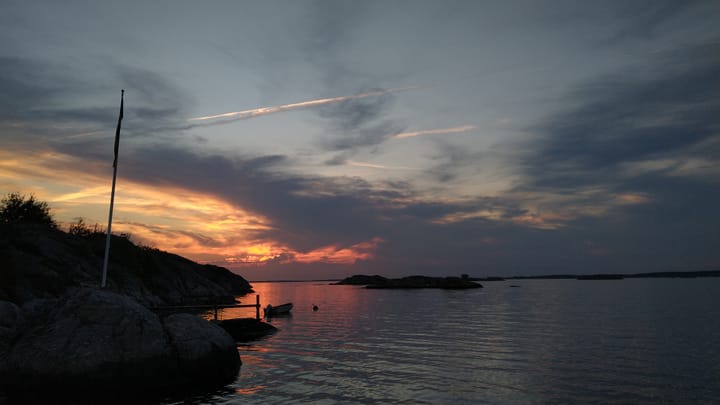 Sunset over a granite outcrop with a flag-pole and Swedish blue and yellow pennant hanging in the calm.