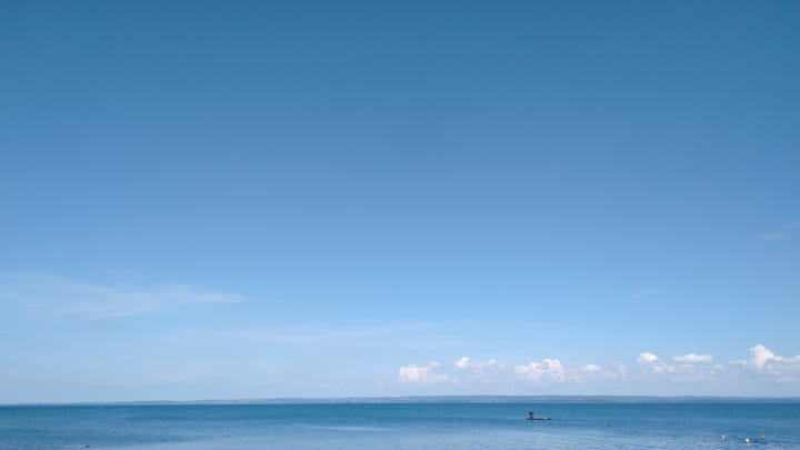 A photo of the sea at Tvätteshallarna, with three swimming-capped swimmers heading towards the pontoon.